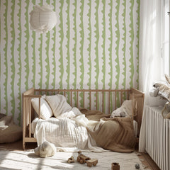 May include: A light wood crib with bedding, including pillows and a blanket, sits on a patterned rug. The room features a white and green striped wallpaper and a paper lantern. Wooden toy cars are on the rug.
